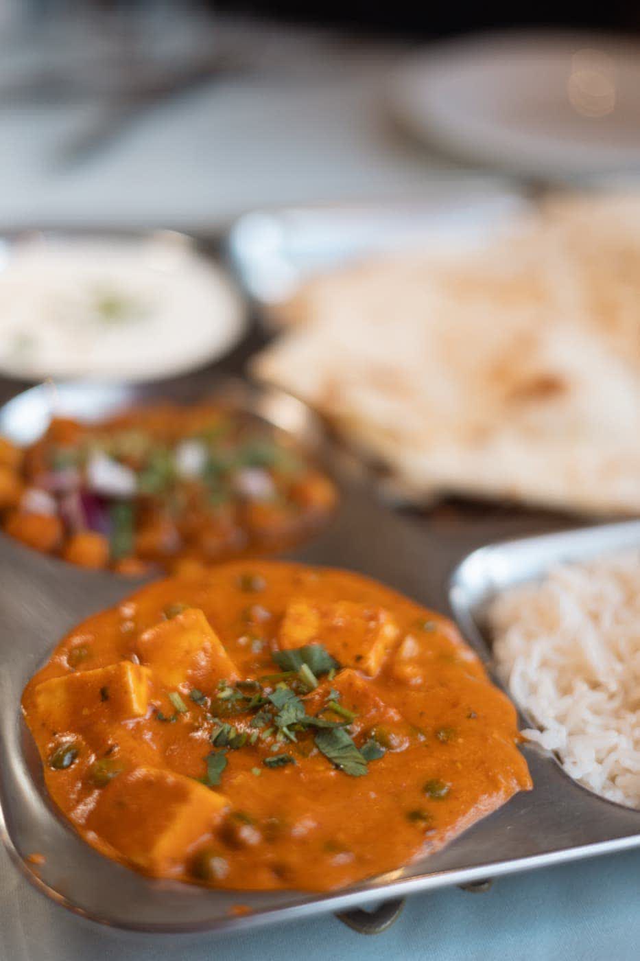 Matar paneer served with rice, naan and channa on a steel thali